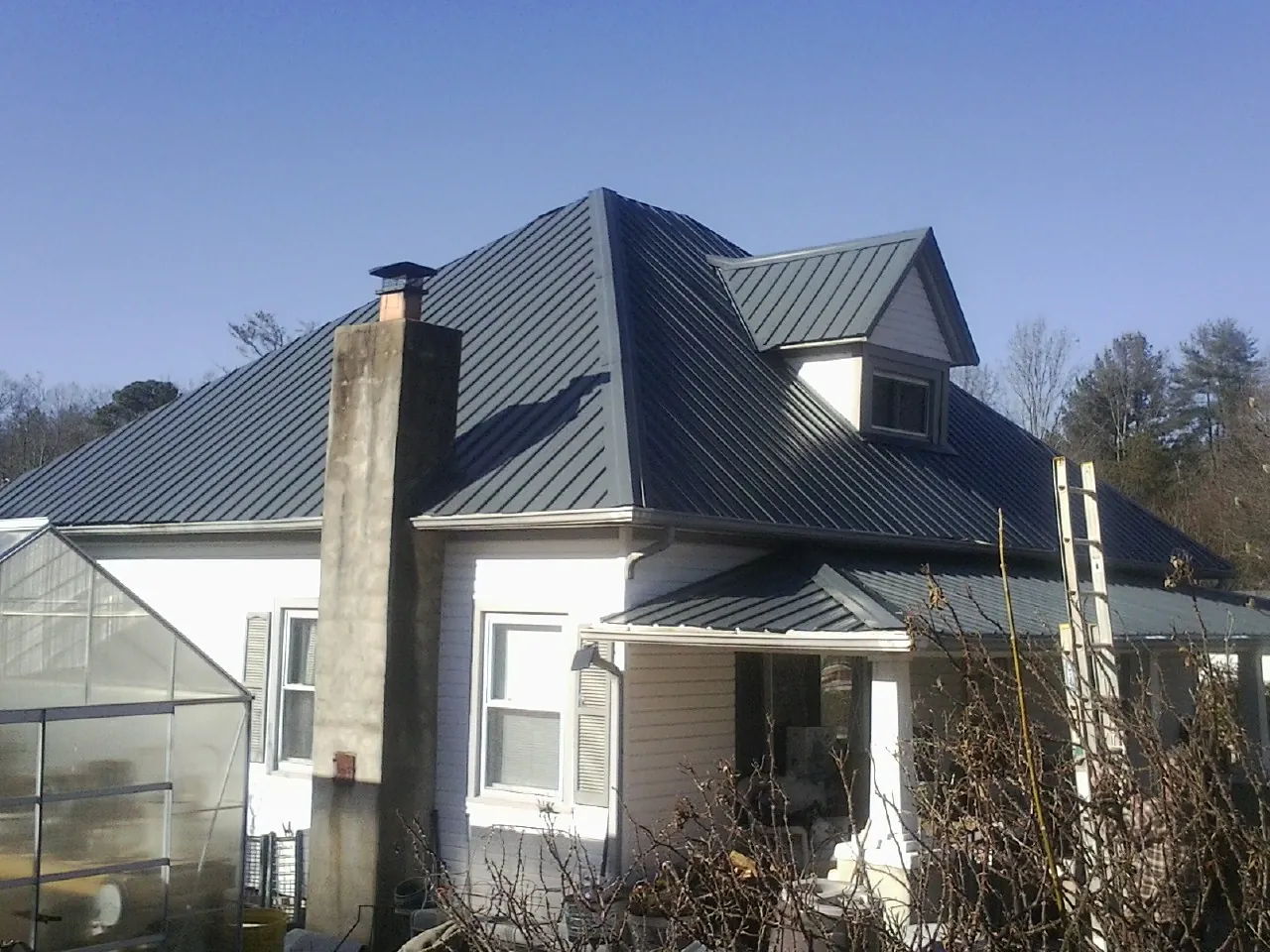Dark blue standing seam metal roof on a white farmhouse with dormer — Slate & Tile Roof Repair by Roofing Brothers in Earlsboro