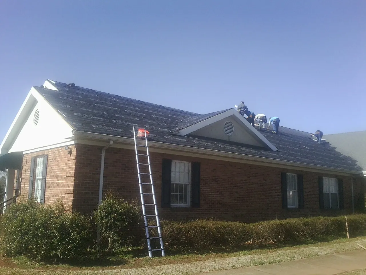 Crew tearing shingles off a brick ranch roof with a ladder set — Emergency Roof Repair work by our crew in Earlsboro