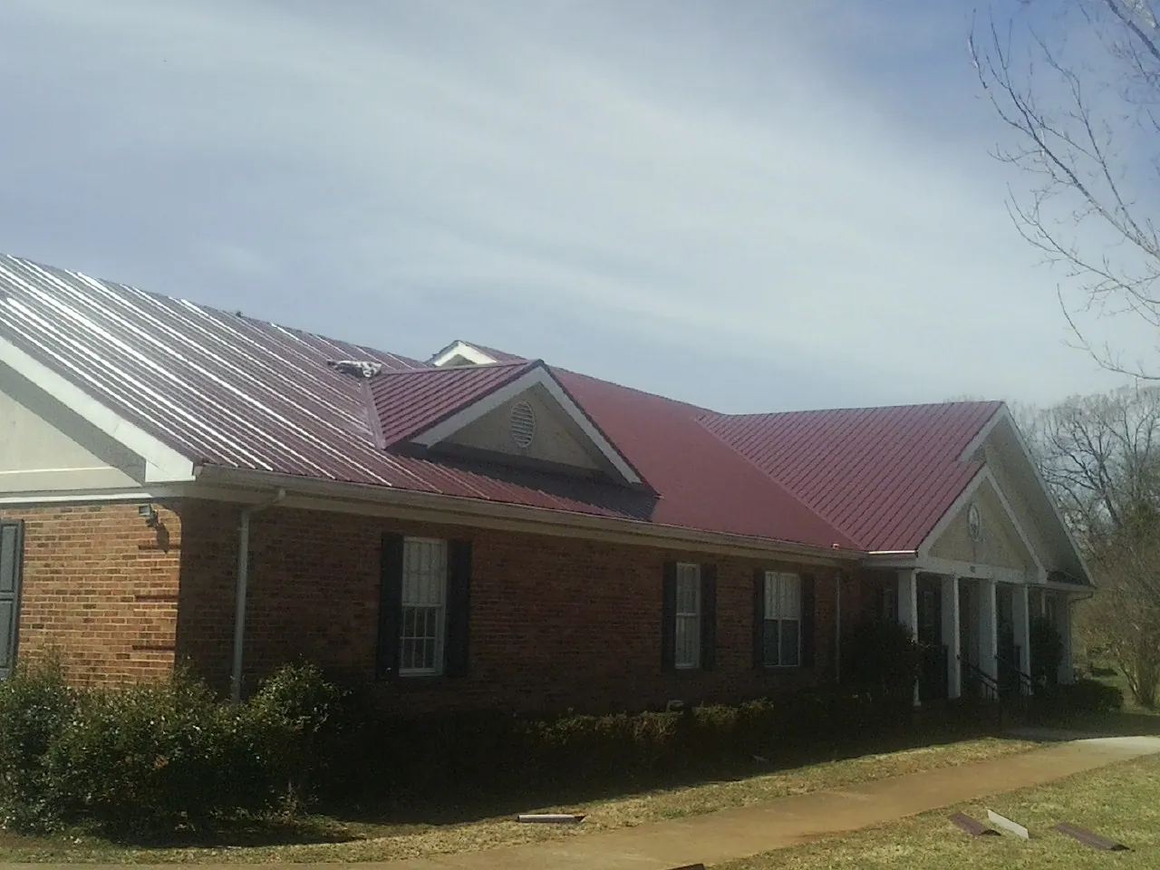 Red metal roof with gabled entries on a long brick building, from a Hail Damage Roof Repair job in Earlsboro