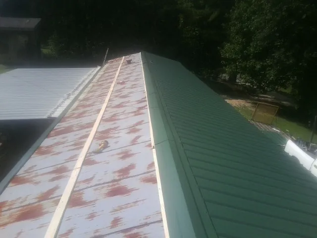 Old rusted panels beside newly installed green metal roofing — Wind Damage Roof Repair by Roofing Brothers in Earlsboro