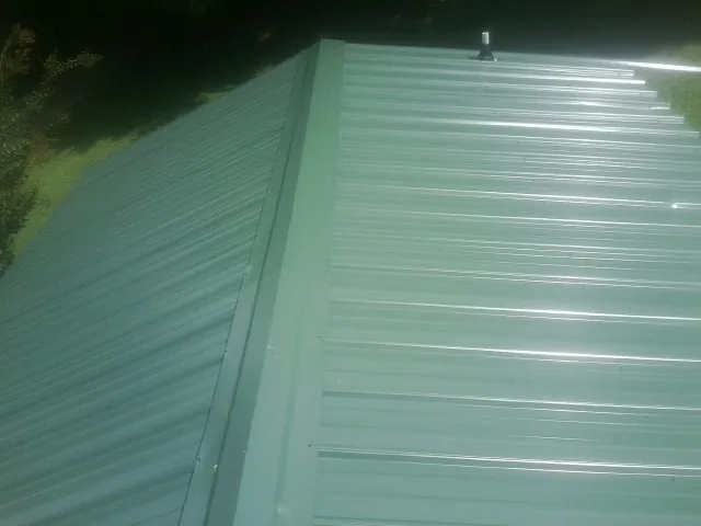New green metal panels meeting at the ridge of a roof — Flat Roof Repair work by our crew in Earlsboro