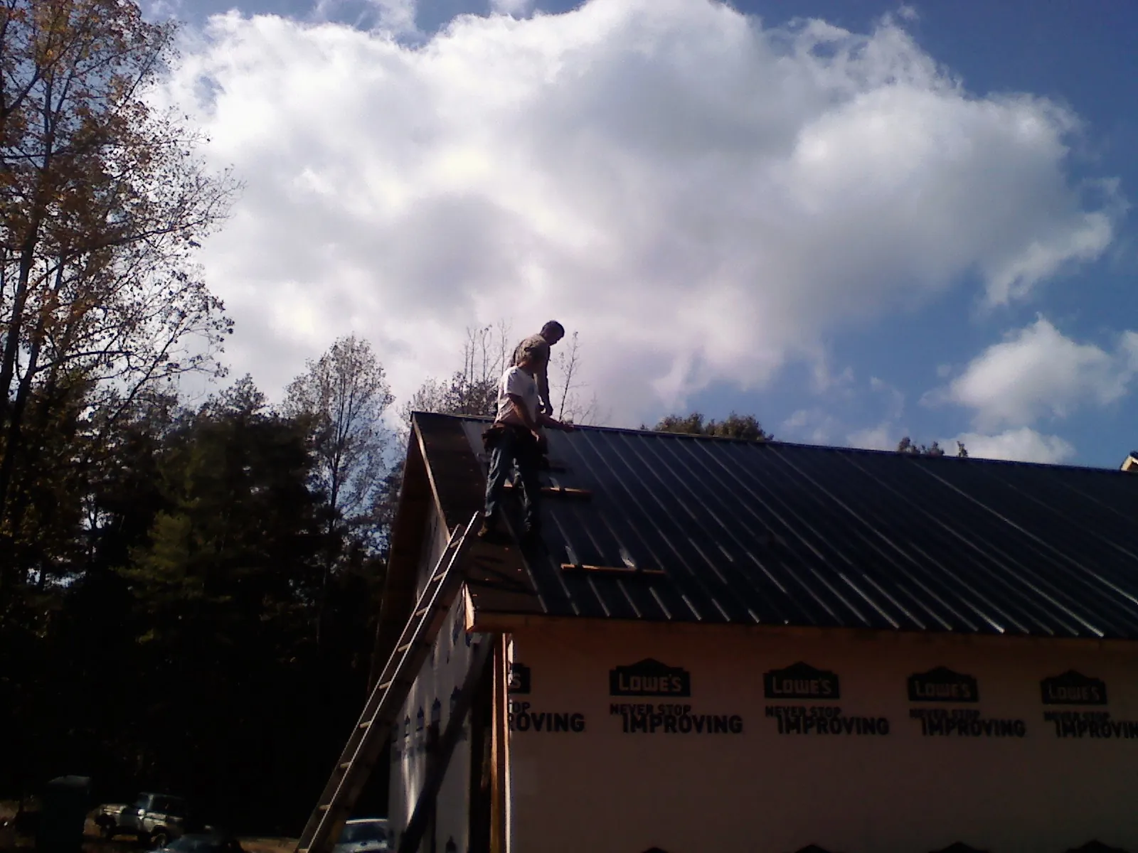 Roofer fastening dark metal panels high against a cloudy sky, from a Roof Inspection job in Earlsboro