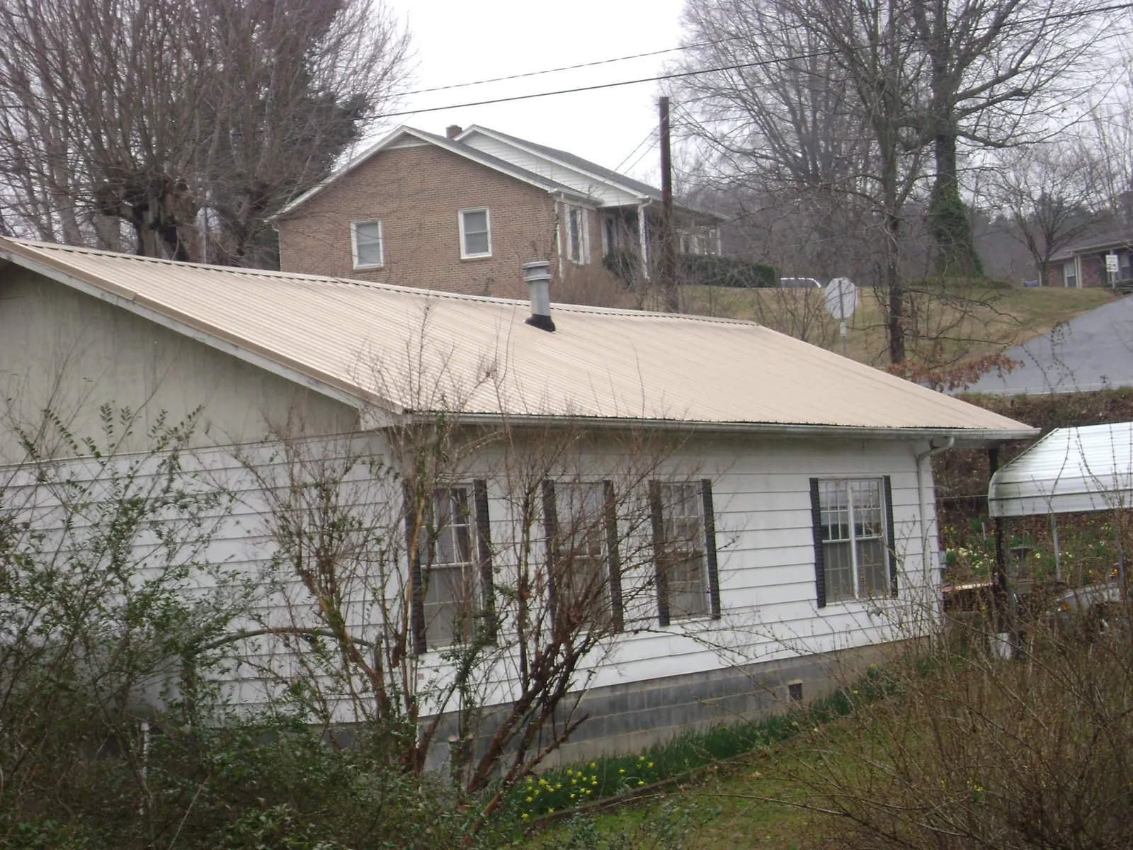 Tan metal roof on a white sided house set into a hillside — Commercial Roofing by Roofing Brothers in Earlsboro