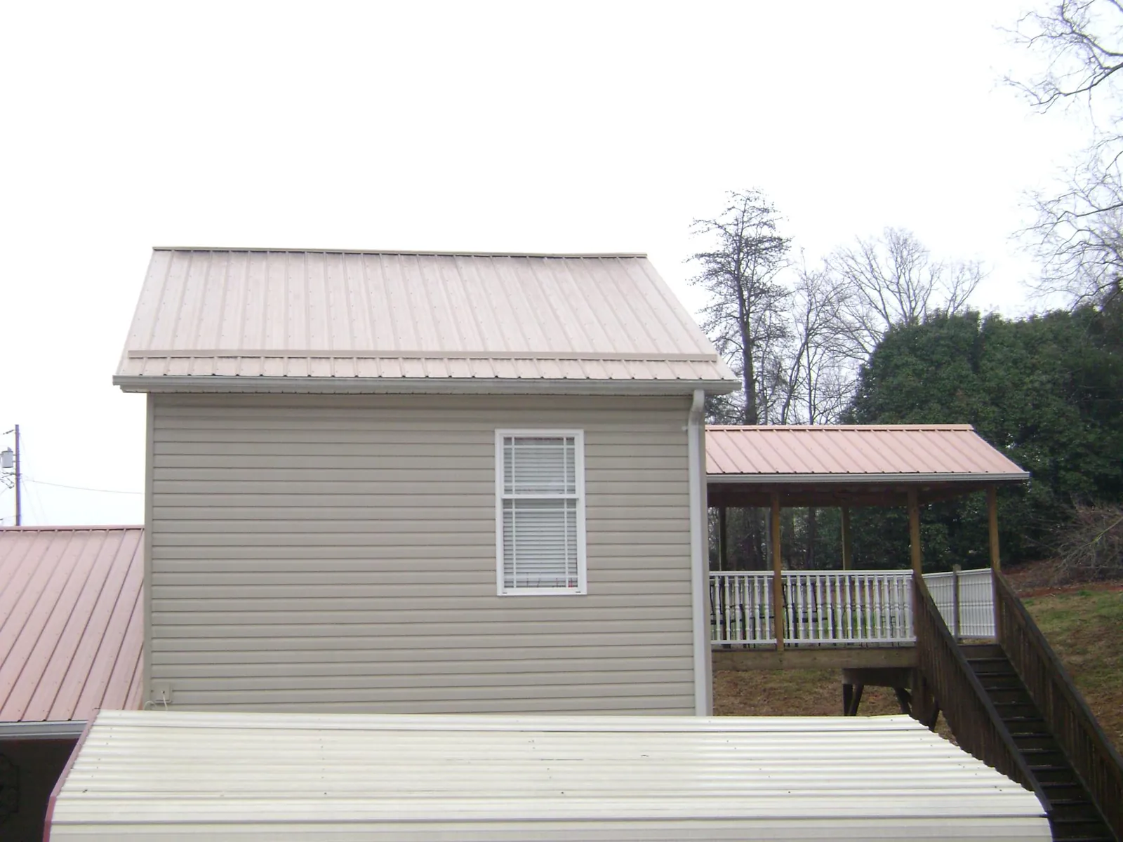 Tan metal roofs on a two story addition and attached porch, from a Roof Replacement job in Earlsboro